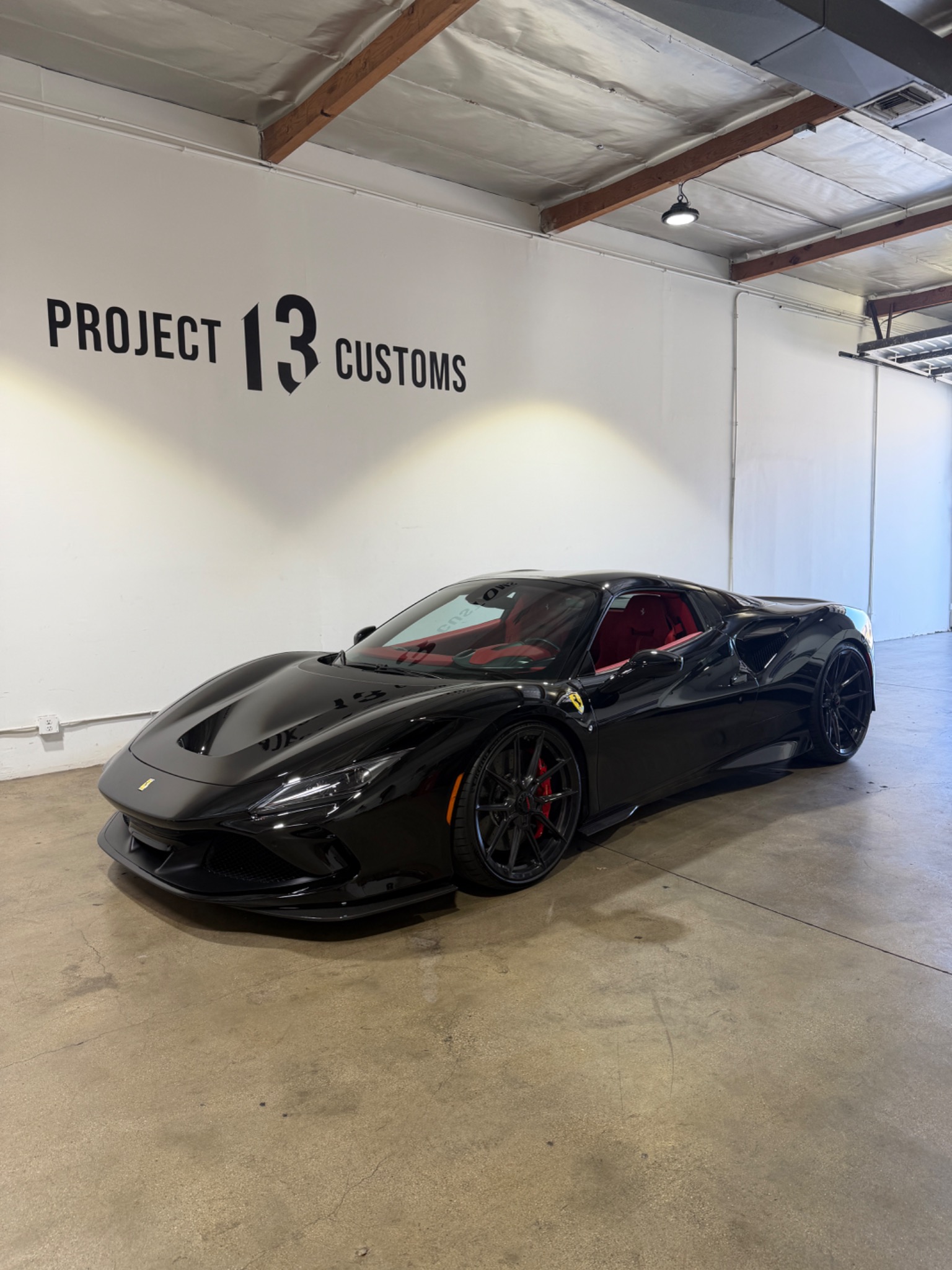 Black Ferrari with red interior beneath the Project 13 Customs wall logo