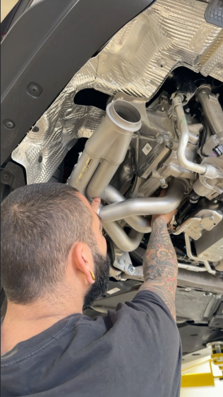 An exhaust system being installed beneath a vehicle at Project 13 Customs