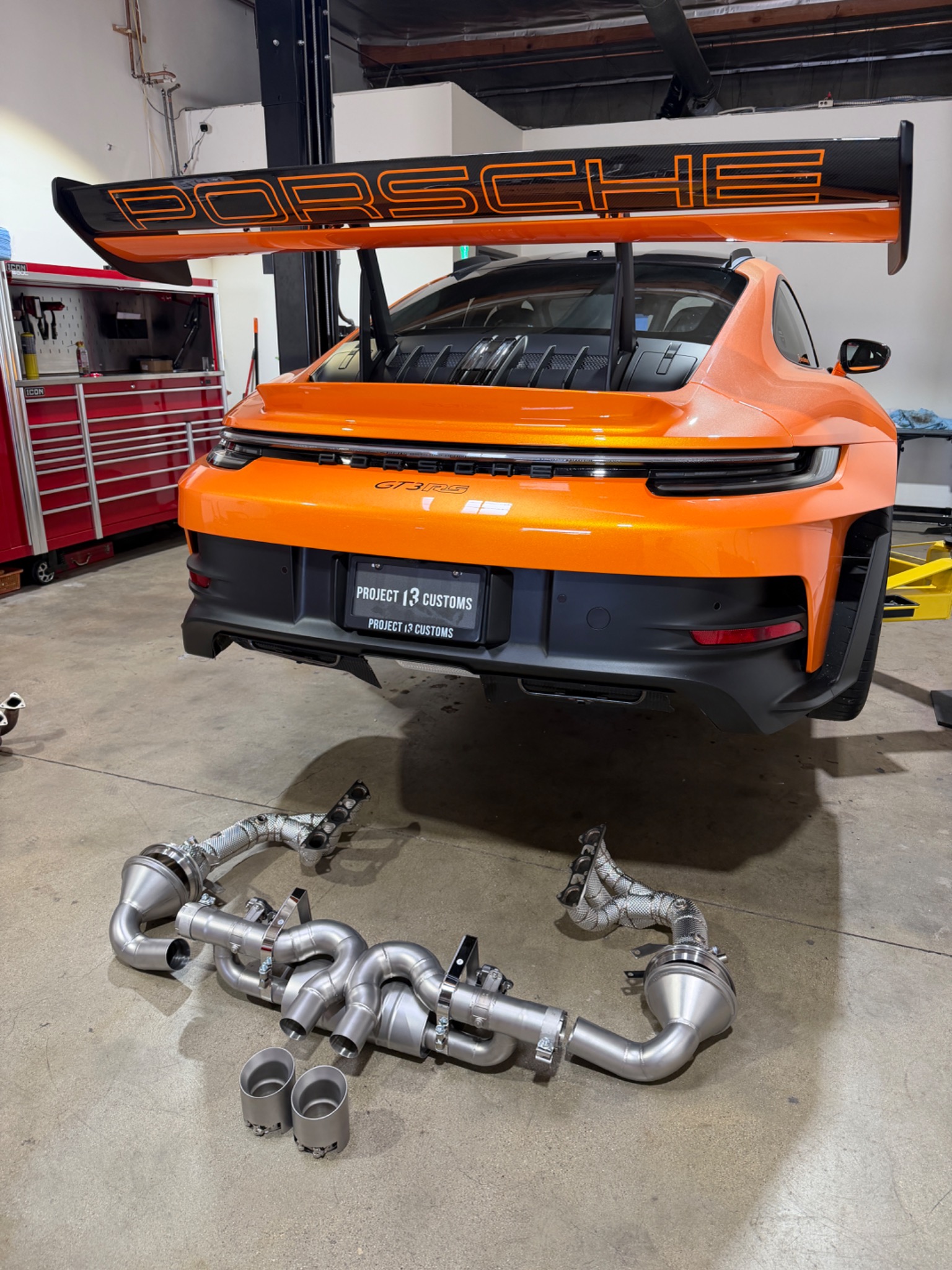 Orange Porsche GT3 RS with an exhaust system displayed in front of the car